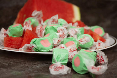 Green-and-pink Watermelon taffy candy from Taffy Town surrounded by juicy watermelon slices - gourmet salt water taffy with a refreshing, nostalgic twist.
